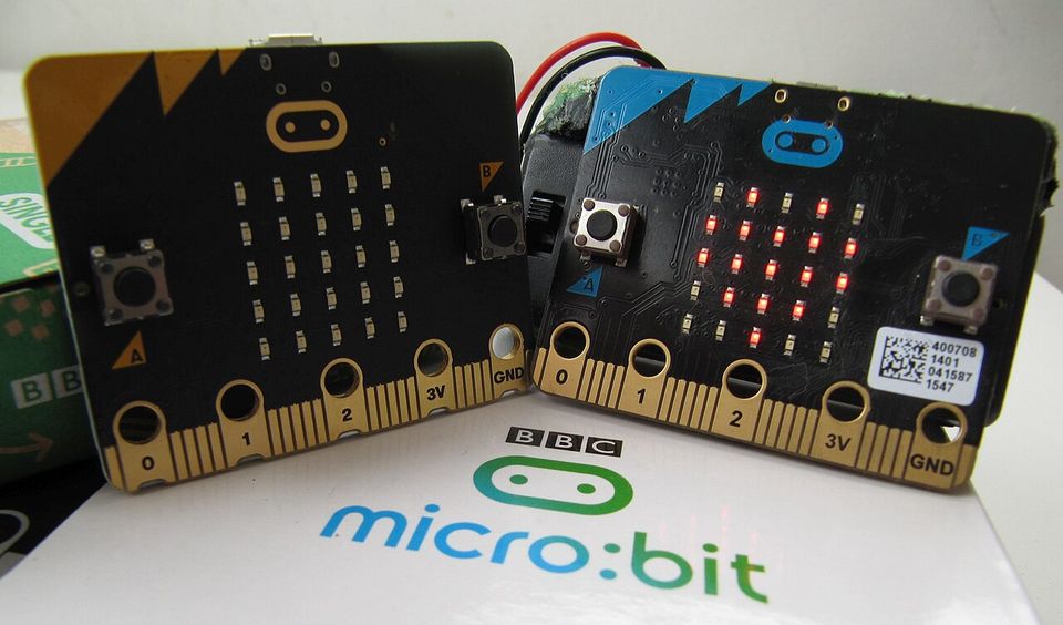 Deux cartes micro:bit vues de face : à gauche une V2 à logo doré, à droite une V1 à logo imprimé. Boutons A et B, 25 LED, bord doré marqué 0, 1, 2, 3V et GND.